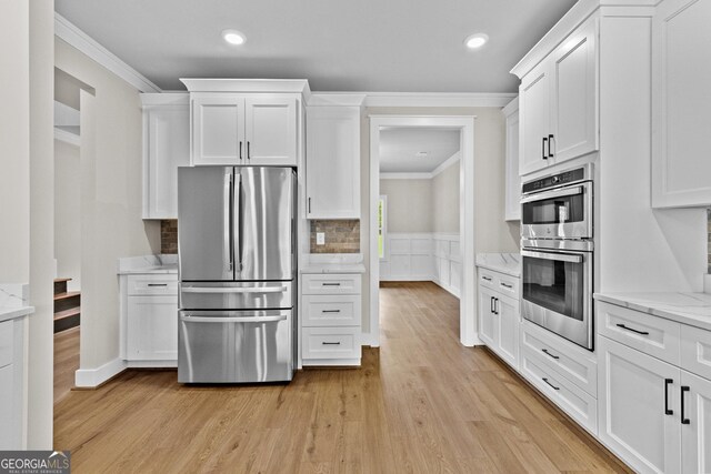 kitchen featuring appliances with stainless steel finishes, light wood-type flooring, white cabinetry, and ornamental molding