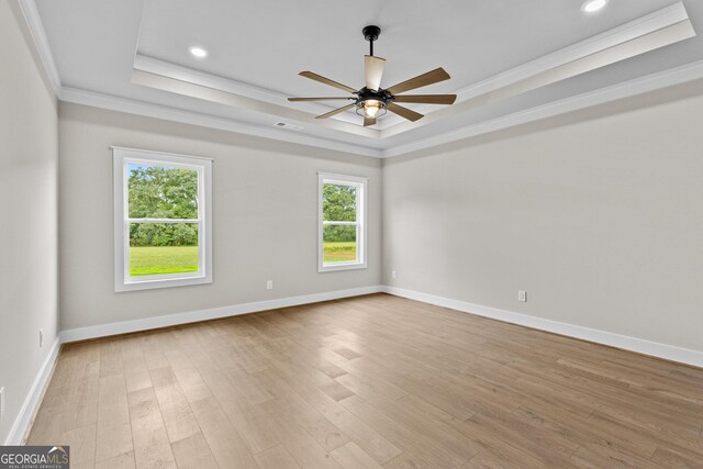 empty room featuring ceiling fan, light wood-type flooring, ornamental molding, and a tray ceiling