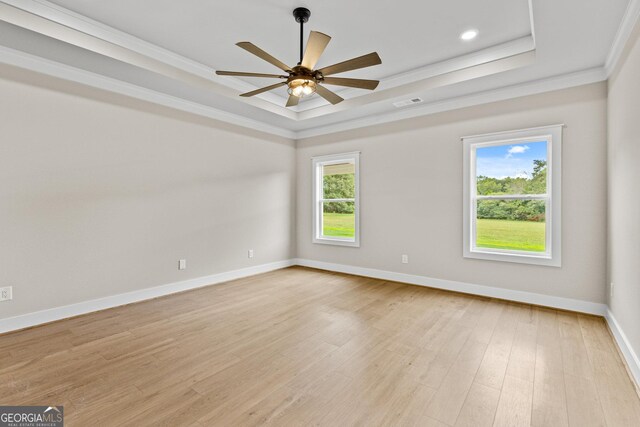 unfurnished room featuring ceiling fan, light wood-type flooring, ornamental molding, and a tray ceiling