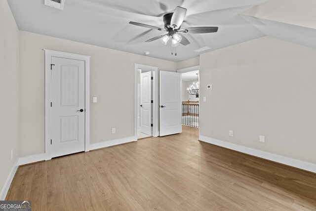 unfurnished bedroom featuring ceiling fan with notable chandelier, light hardwood / wood-style floors, and lofted ceiling