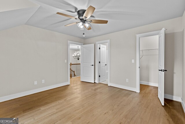 unfurnished bedroom with a walk in closet, a closet, light hardwood / wood-style floors, and ceiling fan with notable chandelier