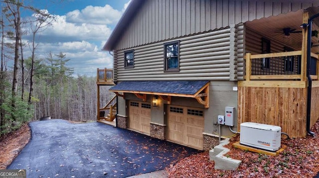 view of side of property with aphalt driveway, log exterior, an attached garage, and a ceiling fan