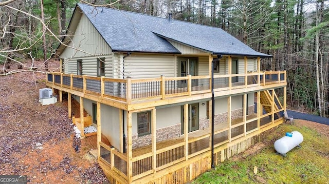 back of house featuring log siding, roof with shingles, a deck, and central air condition unit