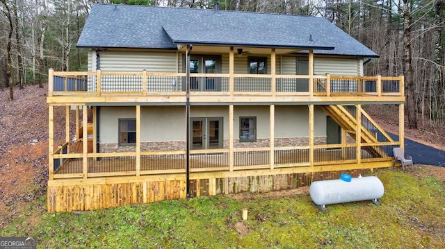 rear view of property with stone siding, stairway, roof with shingles, a wooden deck, and stucco siding