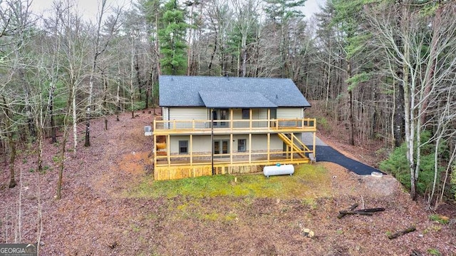 view of front of property featuring a wooded view, roof with shingles, a wooden deck, and driveway