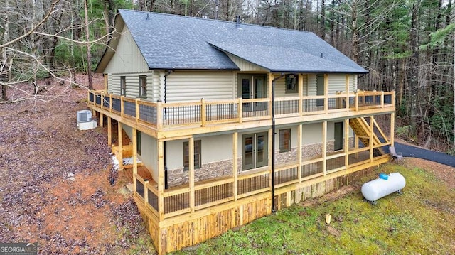 back of house with a deck, central AC unit, and roof with shingles