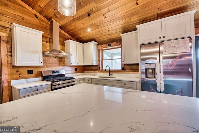 kitchen featuring white cabinetry, sink, wall chimney range hood, pendant lighting, and appliances with stainless steel finishes