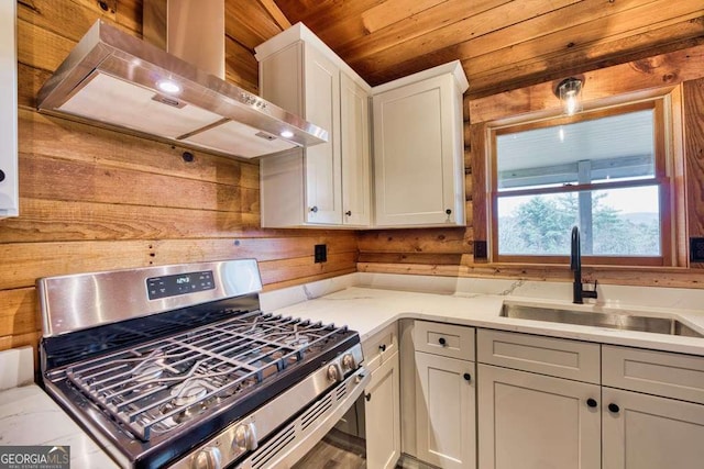 kitchen with stainless steel gas range oven, wall chimney exhaust hood, wood ceiling, sink, and wood walls