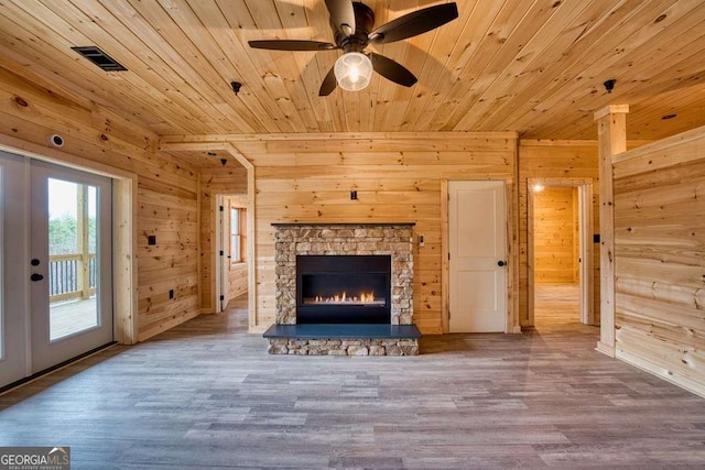 unfurnished living room with wooden ceiling, visible vents, wood finished floors, and a stone fireplace