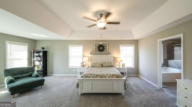 bedroom featuring a tray ceiling, connected bathroom, ceiling fan, and multiple windows