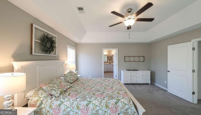 bedroom with a raised ceiling, connected bathroom, ceiling fan, and dark carpet