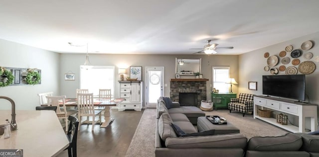 living room featuring ceiling fan, dark hardwood / wood-style floors, and a stone fireplace