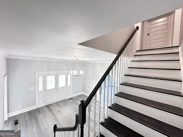 staircase with hardwood / wood-style floors, crown molding, and a notable chandelier