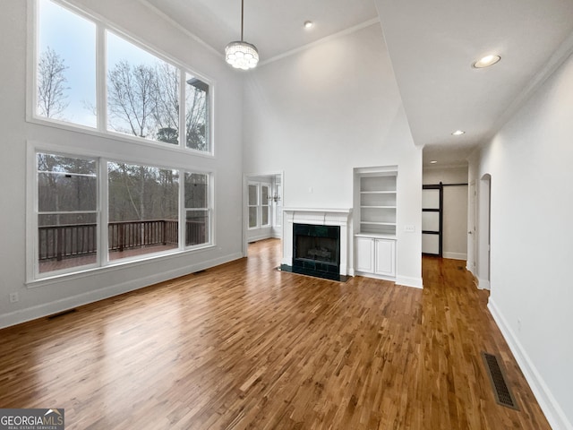 unfurnished living room with a high end fireplace, a towering ceiling, built in features, and a barn door