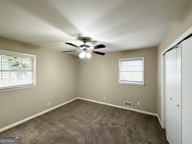 unfurnished bedroom featuring ceiling fan, dark carpet, and a closet