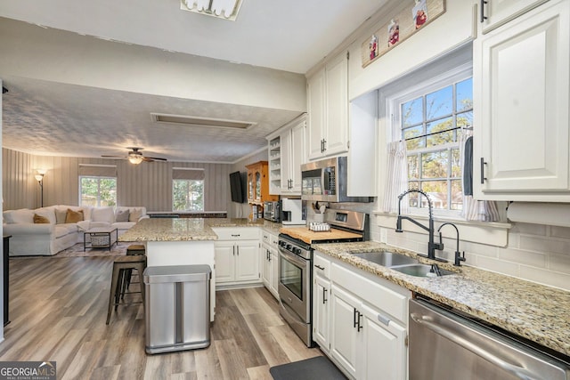 kitchen featuring a kitchen bar, light stone counters, stainless steel appliances, sink, and white cabinets