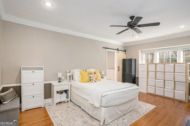 bedroom featuring a barn door, ceiling fan, crown molding, and light wood-type flooring