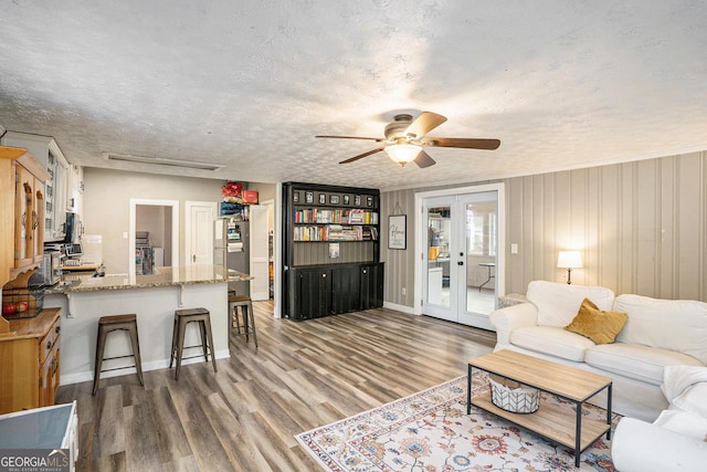 living room with french doors, a textured ceiling, ceiling fan, wooden walls, and dark wood-type flooring