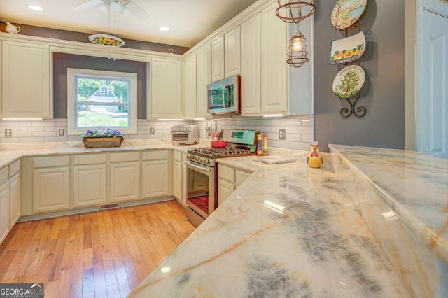 kitchen with hanging light fixtures, stainless steel appliances, tasteful backsplash, light stone counters, and light hardwood / wood-style flooring