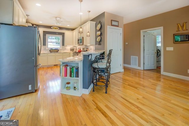 kitchen with appliances with stainless steel finishes, a kitchen breakfast bar, light hardwood / wood-style flooring, white cabinetry, and hanging light fixtures