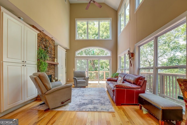 living room with ceiling fan, light hardwood / wood-style floors, a towering ceiling, and a wealth of natural light