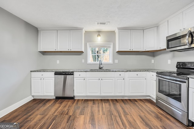 kitchen featuring sink, dark hardwood / wood-style flooring, dark stone countertops, white cabinets, and appliances with stainless steel finishes