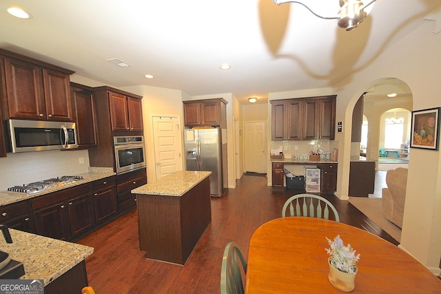 kitchen with dark wood-type flooring, tasteful backsplash, light stone counters, a kitchen island, and appliances with stainless steel finishes