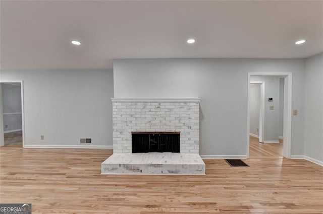 unfurnished living room featuring light wood-type flooring and a brick fireplace