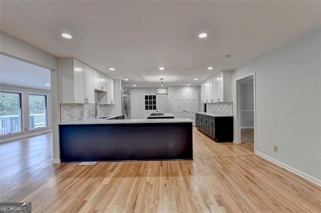 kitchen featuring backsplash, white cabinets, sink, light hardwood / wood-style flooring, and kitchen peninsula