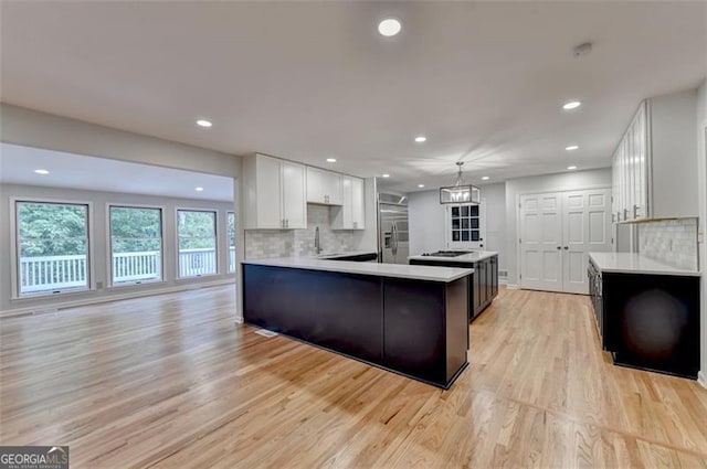 kitchen featuring hanging light fixtures, tasteful backsplash, light hardwood / wood-style floors, stainless steel built in fridge, and white cabinets