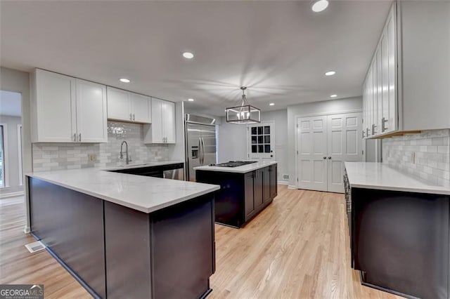 kitchen featuring a center island, built in fridge, white cabinets, hanging light fixtures, and stovetop