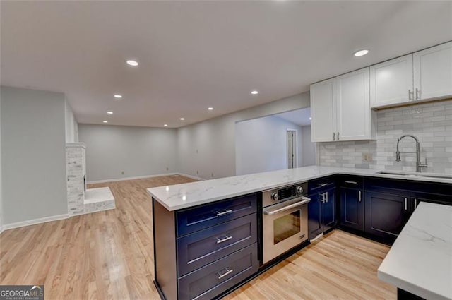 kitchen featuring stainless steel oven, backsplash, sink, light stone countertops, and white cabinetry