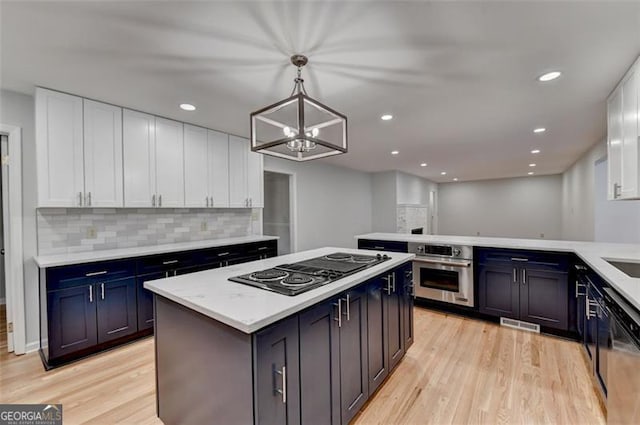 kitchen with a center island, white cabinets, tasteful backsplash, decorative light fixtures, and stainless steel appliances