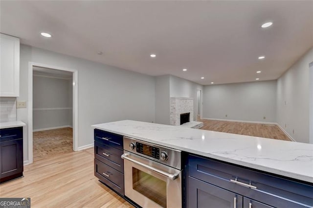 kitchen with decorative backsplash, light wood-type flooring, light stone counters, a brick fireplace, and stainless steel oven