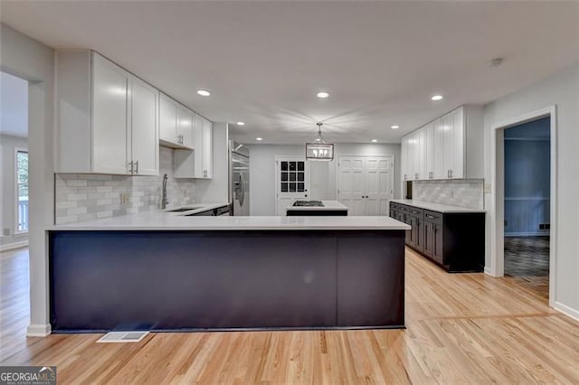 kitchen with backsplash, kitchen peninsula, white cabinetry, and light hardwood / wood-style floors