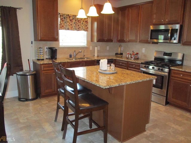 kitchen featuring sink, light stone countertops, decorative light fixtures, a kitchen island, and stainless steel appliances