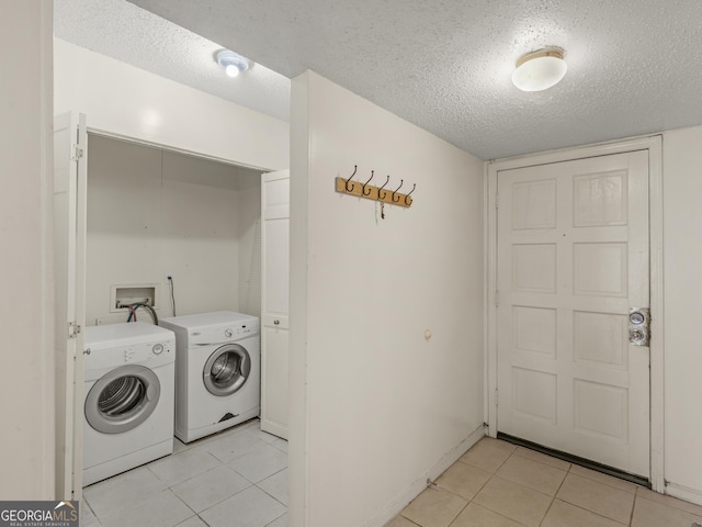 washroom with a textured ceiling, washing machine and dryer, and light tile patterned floors