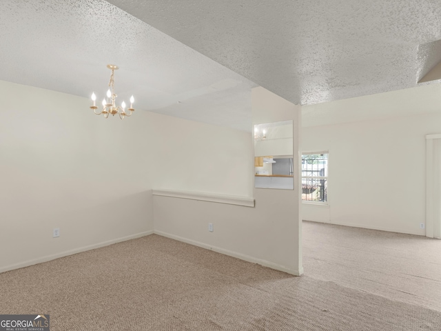 spare room featuring a chandelier, a textured ceiling, and light colored carpet