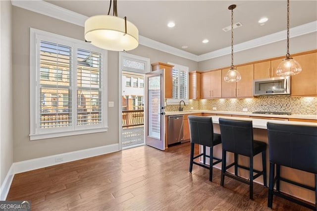 kitchen featuring light brown cabinets, hanging light fixtures, crown molding, a kitchen bar, and appliances with stainless steel finishes