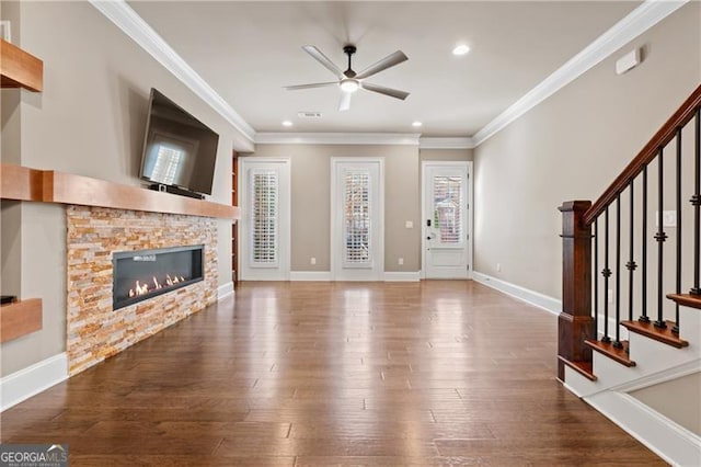 unfurnished living room featuring ceiling fan, a stone fireplace, ornamental molding, and wood-type flooring