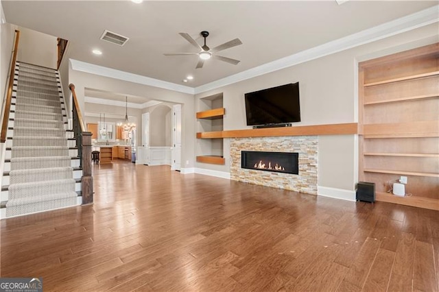 unfurnished living room featuring built in shelves, crown molding, a fireplace, and ceiling fan with notable chandelier