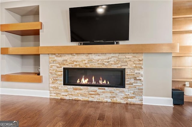 interior details featuring built in shelves, a stone fireplace, and hardwood / wood-style floors