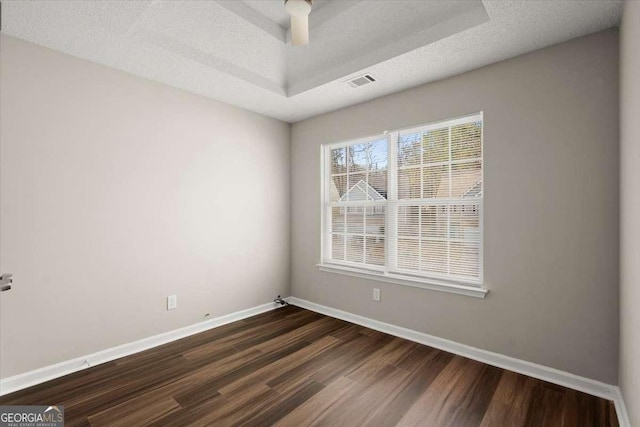 unfurnished room featuring a tray ceiling, dark hardwood / wood-style flooring, and a textured ceiling