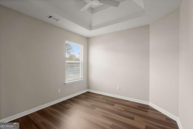 empty room featuring a tray ceiling, ceiling fan, dark hardwood / wood-style flooring, and a textured ceiling