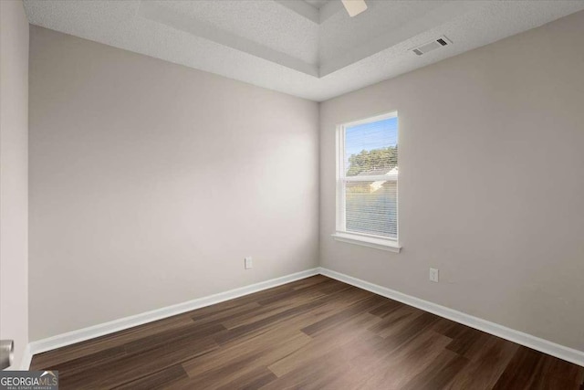 empty room with a textured ceiling, dark wood-type flooring, and a tray ceiling