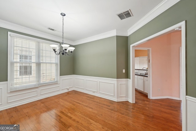 unfurnished dining area featuring a sink, wood finished floors, visible vents, and a notable chandelier