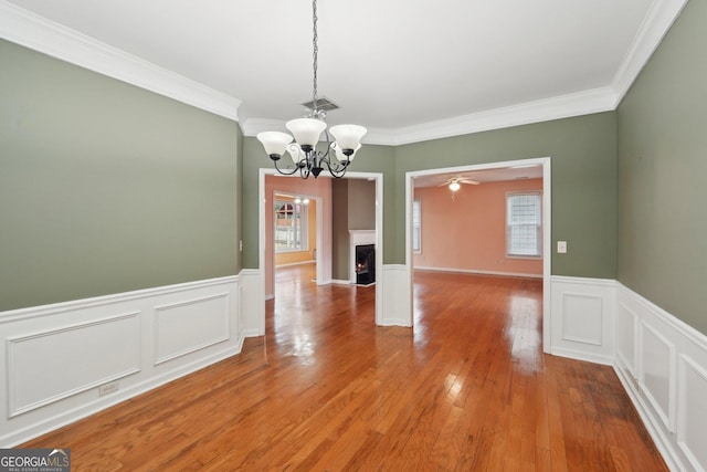 unfurnished dining area with crown molding, visible vents, wainscoting, wood finished floors, and a lit fireplace