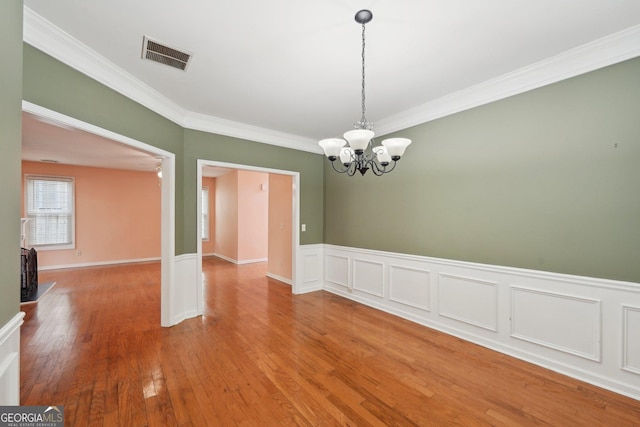 unfurnished dining area featuring crown molding, wood finished floors, visible vents, and an inviting chandelier