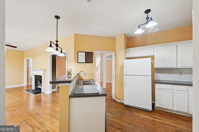 kitchen with dark countertops, a sink, freestanding refrigerator, and white cabinets