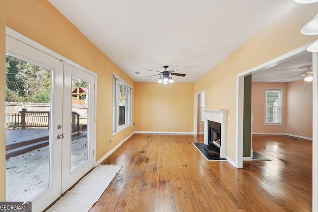 unfurnished living room featuring french doors, wood finished floors, a glass covered fireplace, and baseboards